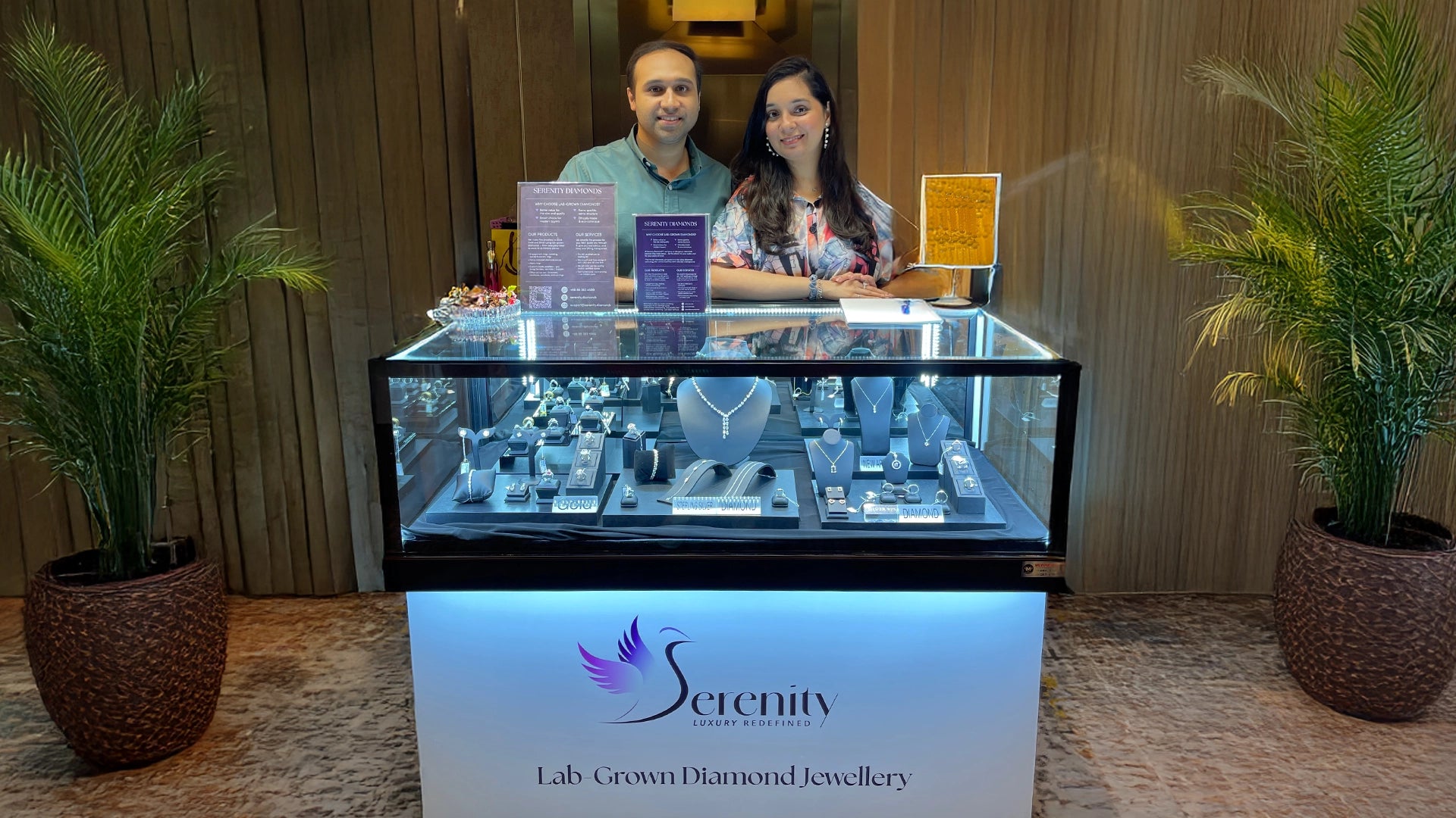 Two people standing behind a display case with 'Serenity' jewelry branding.